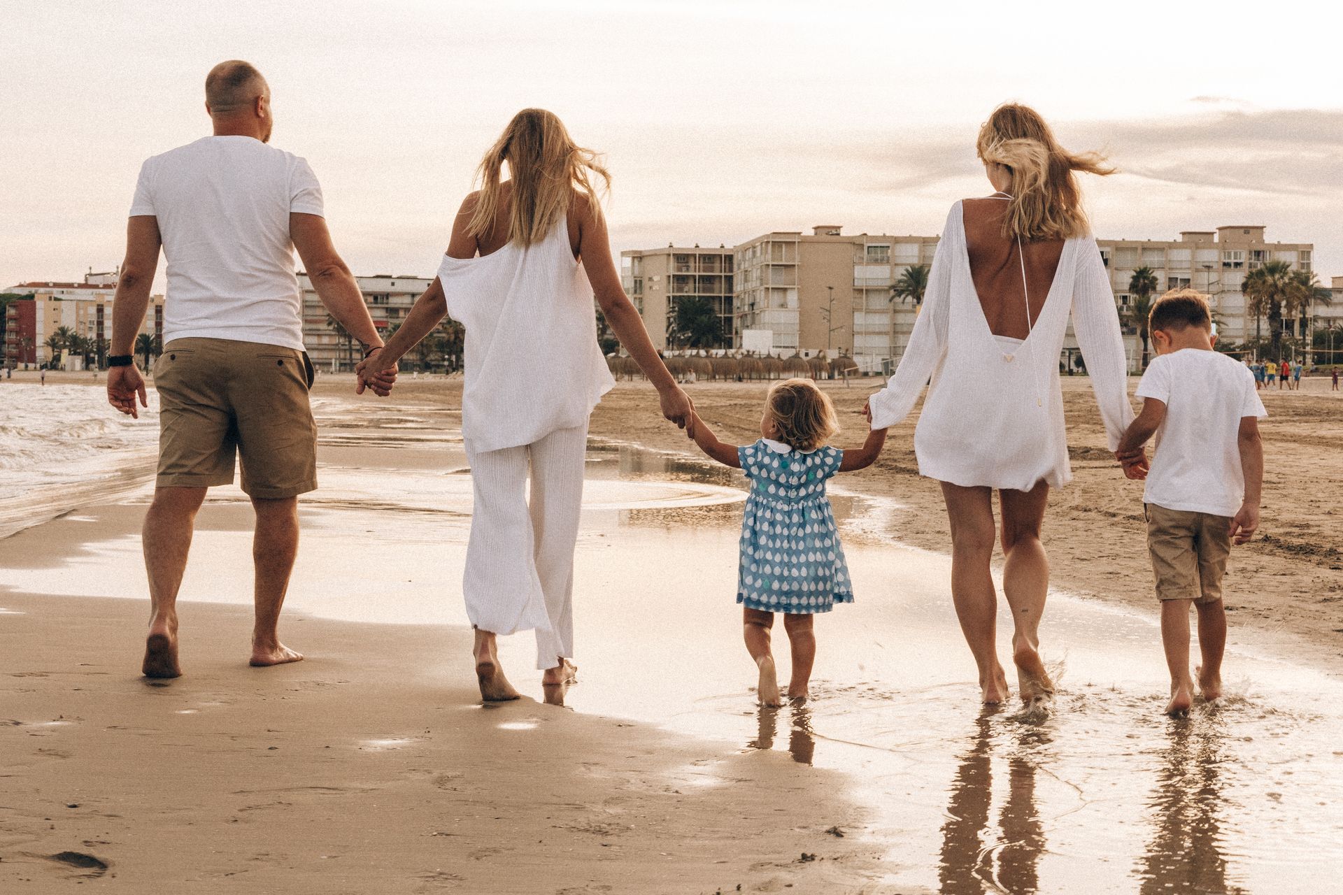 A family walking hand in hand along the shoreline at golden hour